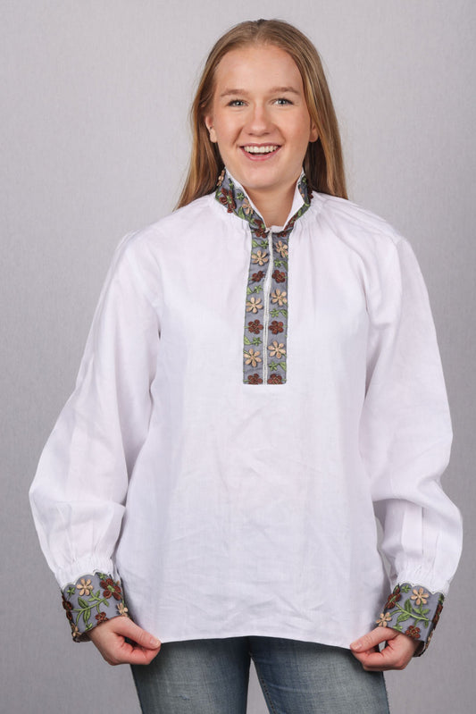 Kritthvit lerretsbomullsskjorte med nydelige detaljer på hals og ermene. Det er brukt broderibånd med nydelige farger. Skjorten kan brukes til forskjellige festdrakt og bunad.