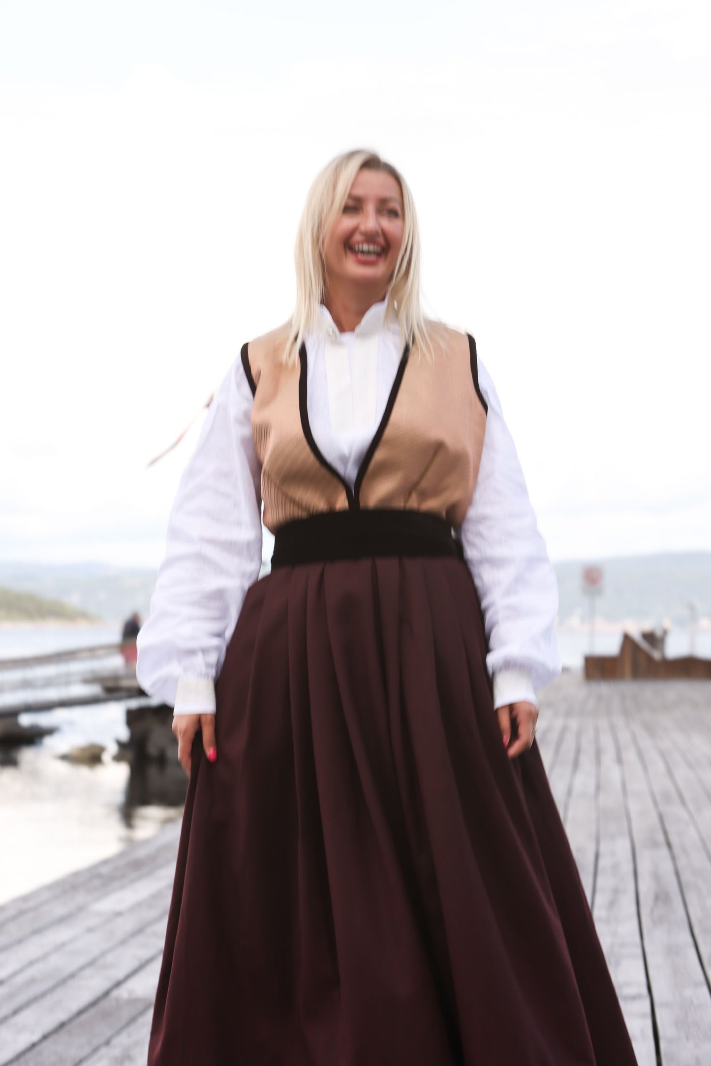 Festdrakt i 100% fin og lett ull i dyp vinrød farge. Stakken er avsluttet med 10 cm velur kant og har en bred tilhørende belte i velur. Livet består av silke. Komplett drakt består av 3 deler, stakk, belte og hvit bunadsskjorte i bomull. Bildet viser helfigur.