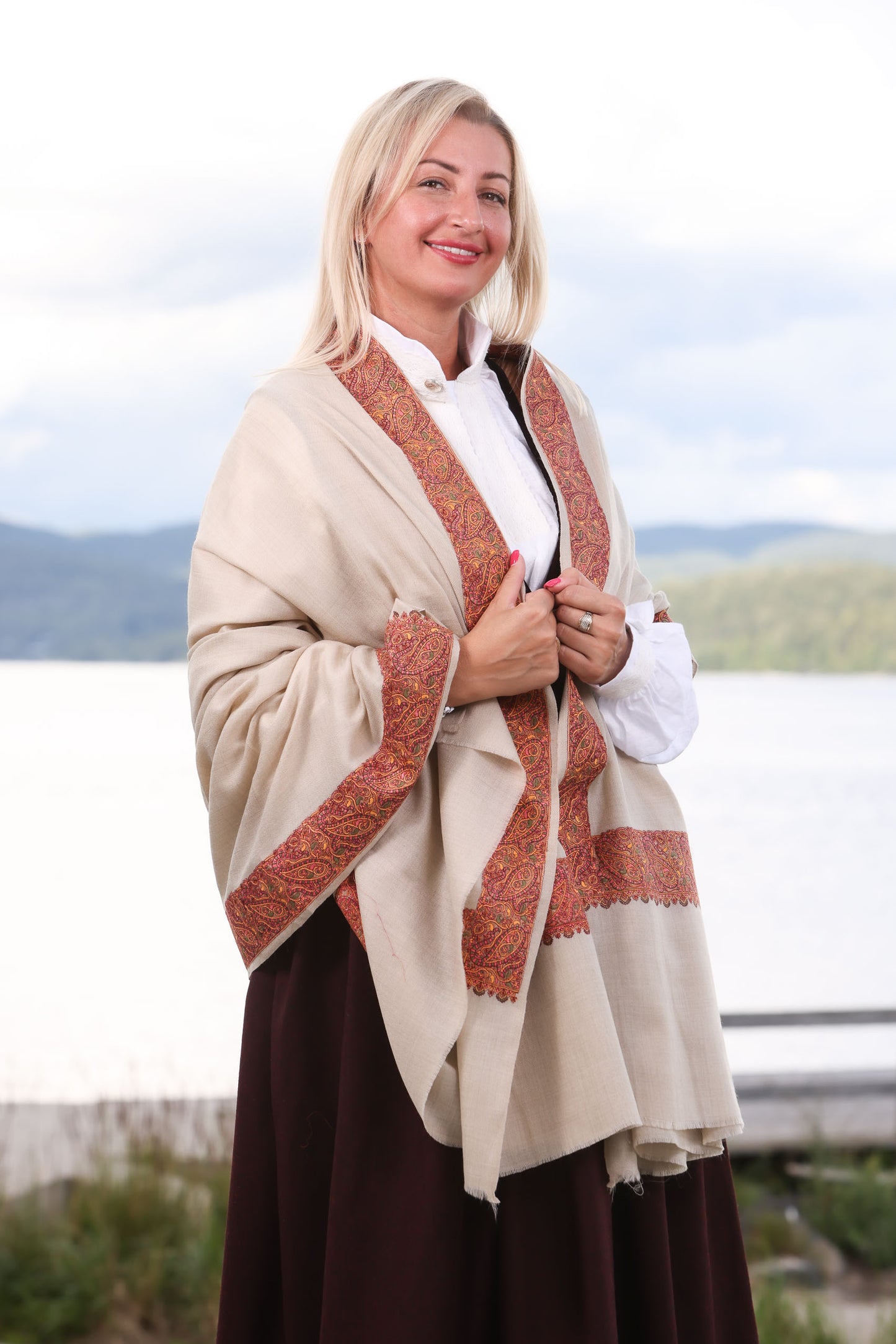 Sjalet Blomstereng er inspirert av norske skog og marker. Sjalet laget i fineste Kashmir ull som florlett og likevel varm og god. Sjalet kan brukes til både til hverdags og fest. Bildet viser sjalet i beige farge.