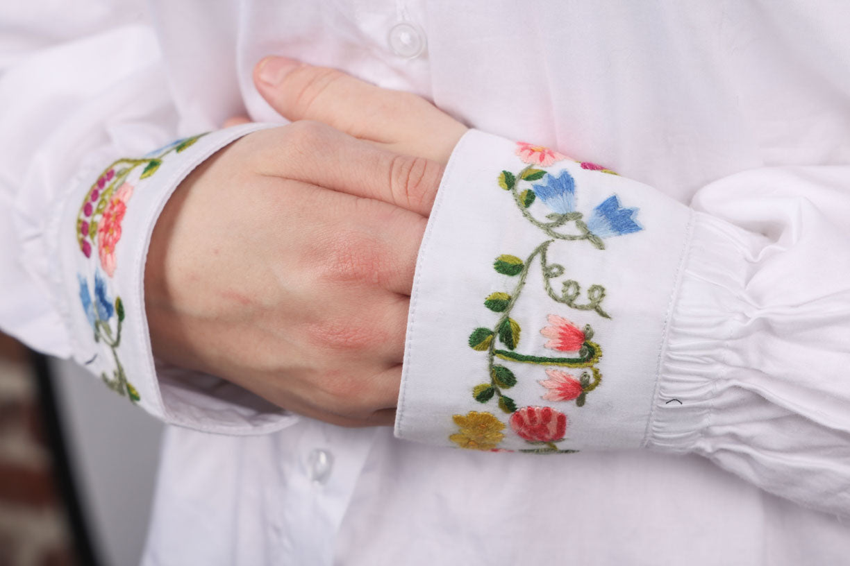 Håndbrodert skjorte i strykelett bomull. Skjorten er håndbrodert med nydelige blomster fra den norske flora. Håndbrodert skjorte med fyldig blomsterlenke på krage og ermene. Bildet viser detaljer på ermene.